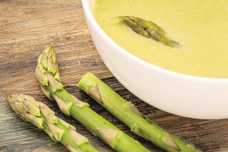 A bowl of asparagus cream soup with green asparagus spears