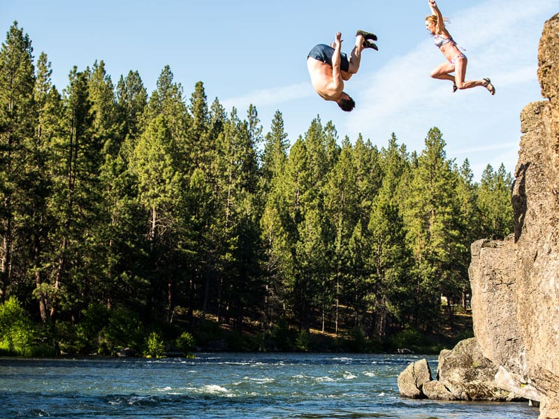 Two people jumping from a rock into water