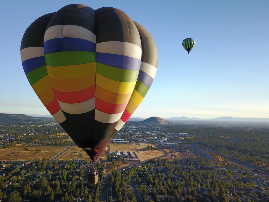 Two hot air balloons flying over Bend, Oregon with Pilot Butte in the background.