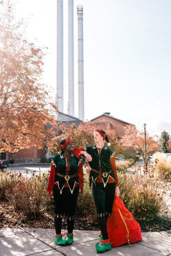 Two people dressed like Santa's helpers outside in the Old Mill District