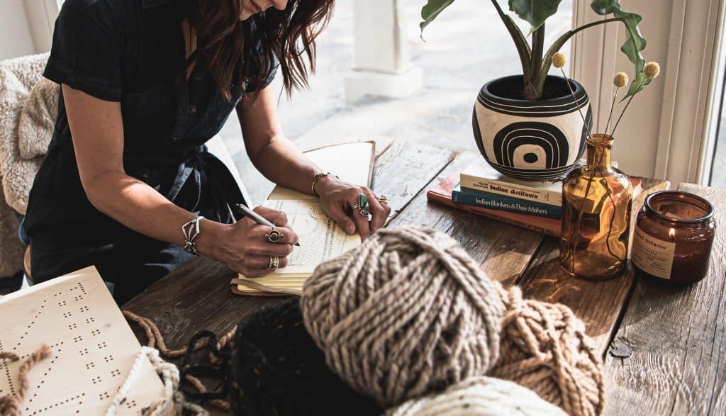 Woman writing with yarn and books nearby