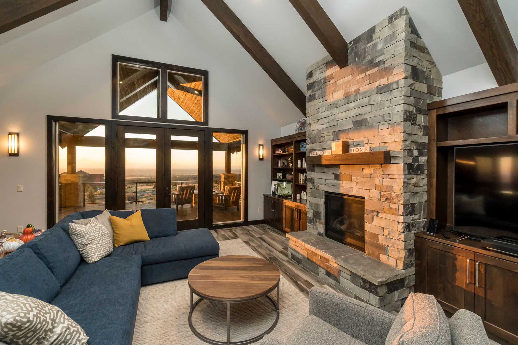 Large living room with a stone fireplace. Open windows with the sun setting outside