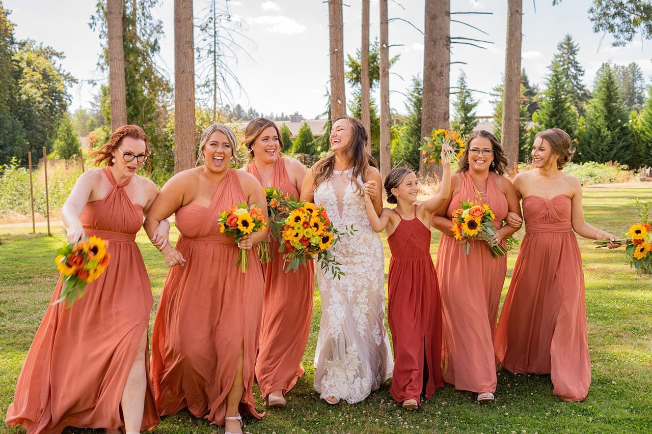 Bride and bridesmaids laughing with flowers outside.