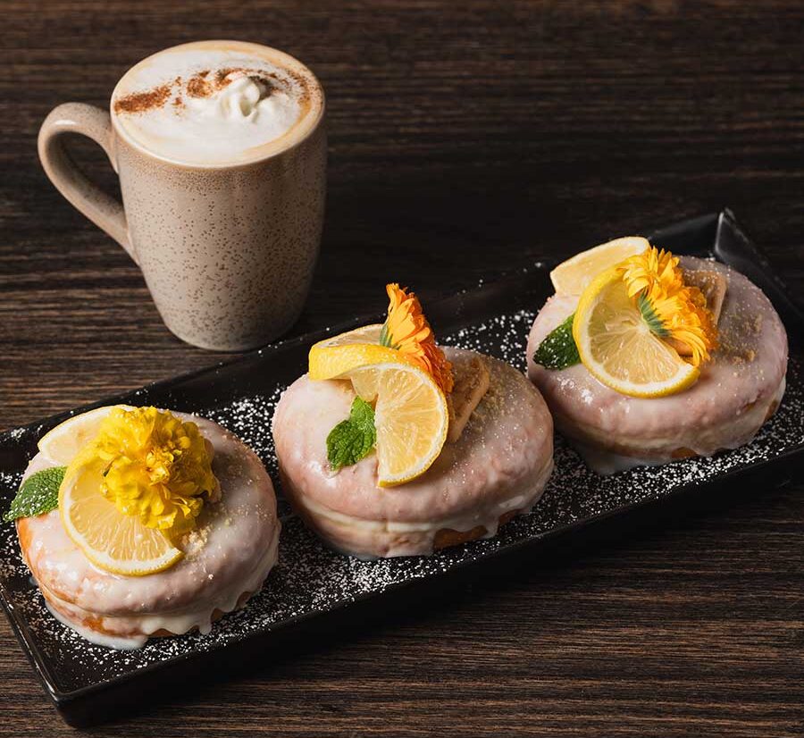 Handmade donuts with edible flowers on a plate with a latte at Brand 44°