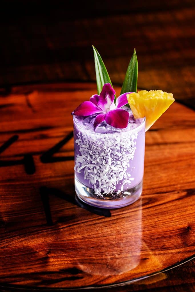 Purple cocktail with salted rim on table.