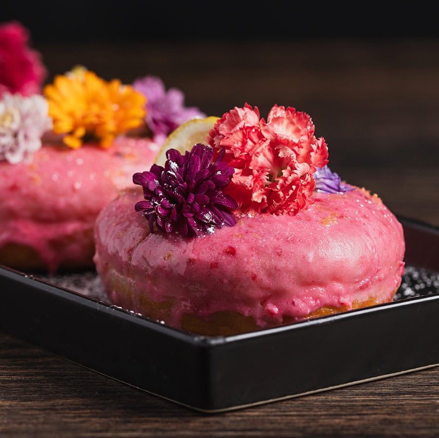 Pink handmade donuts by Brand 44 with edible flowers on top.