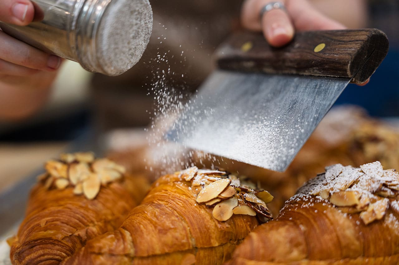 Powdered sugar dusted onto fresh croissant at M's Bakery