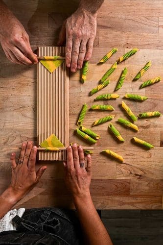 handmade yellow and green pasta being rolled into shape