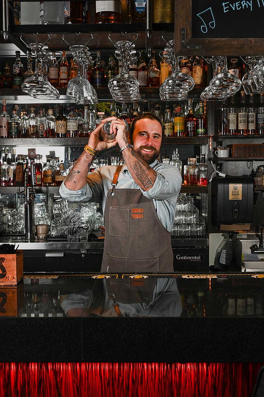 Bartender shaking drink in shaker in front of mirrored bar wall