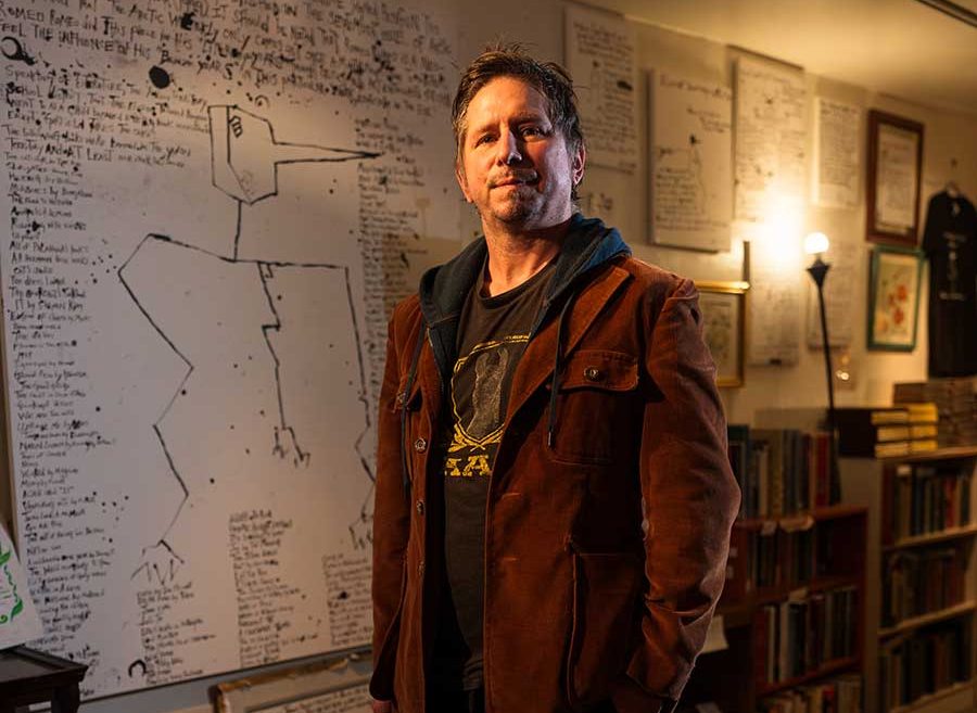 Justin Schlosberg poses in front of white board with text and images on it.