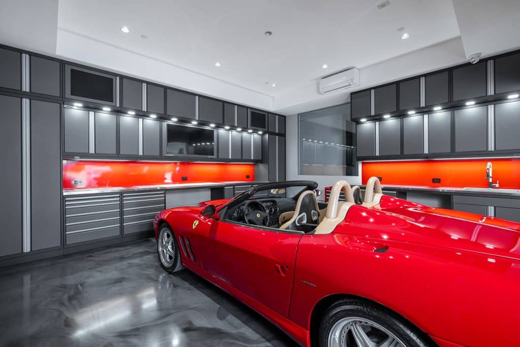 Red car in garage with polished floor and extensive grey cabinets and storage options