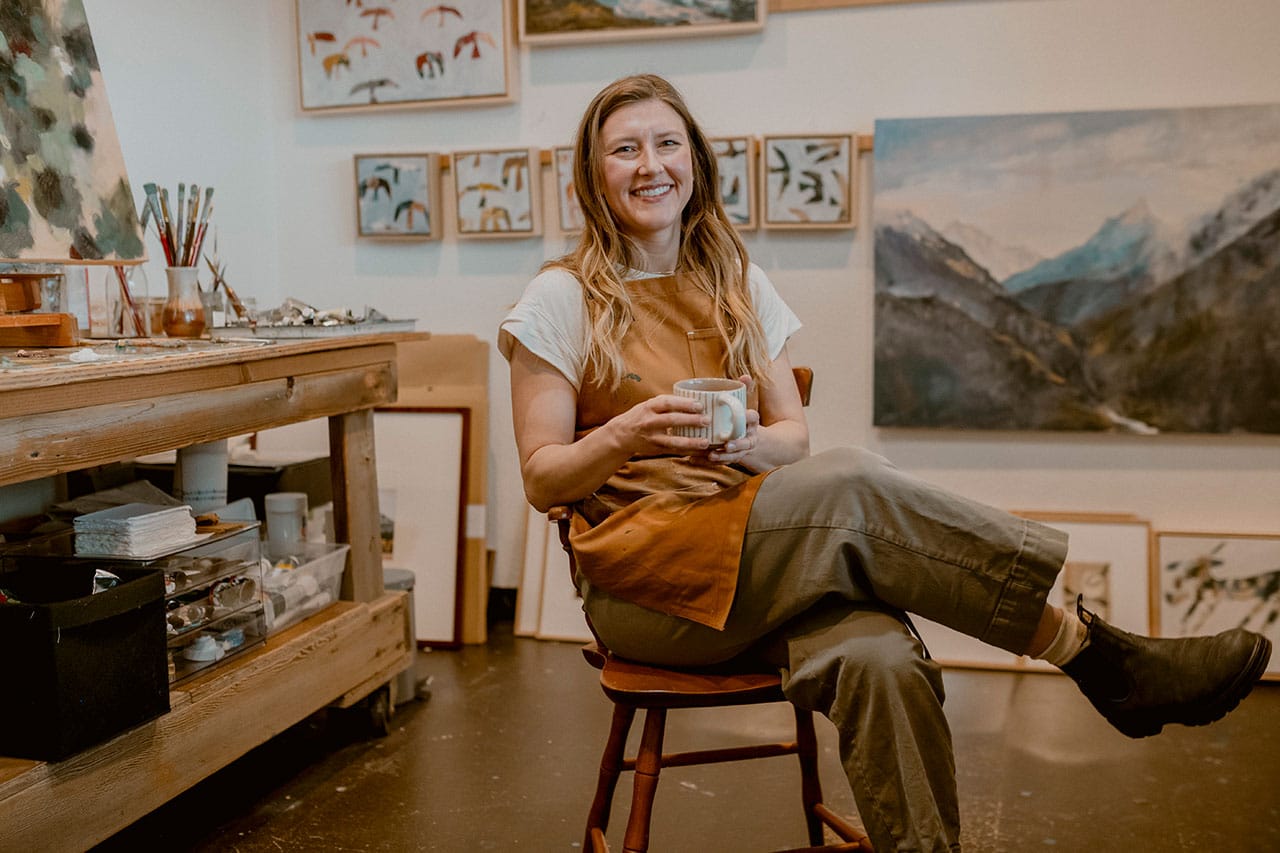 Jen McCaffrey sitting and holding coffee in her studio