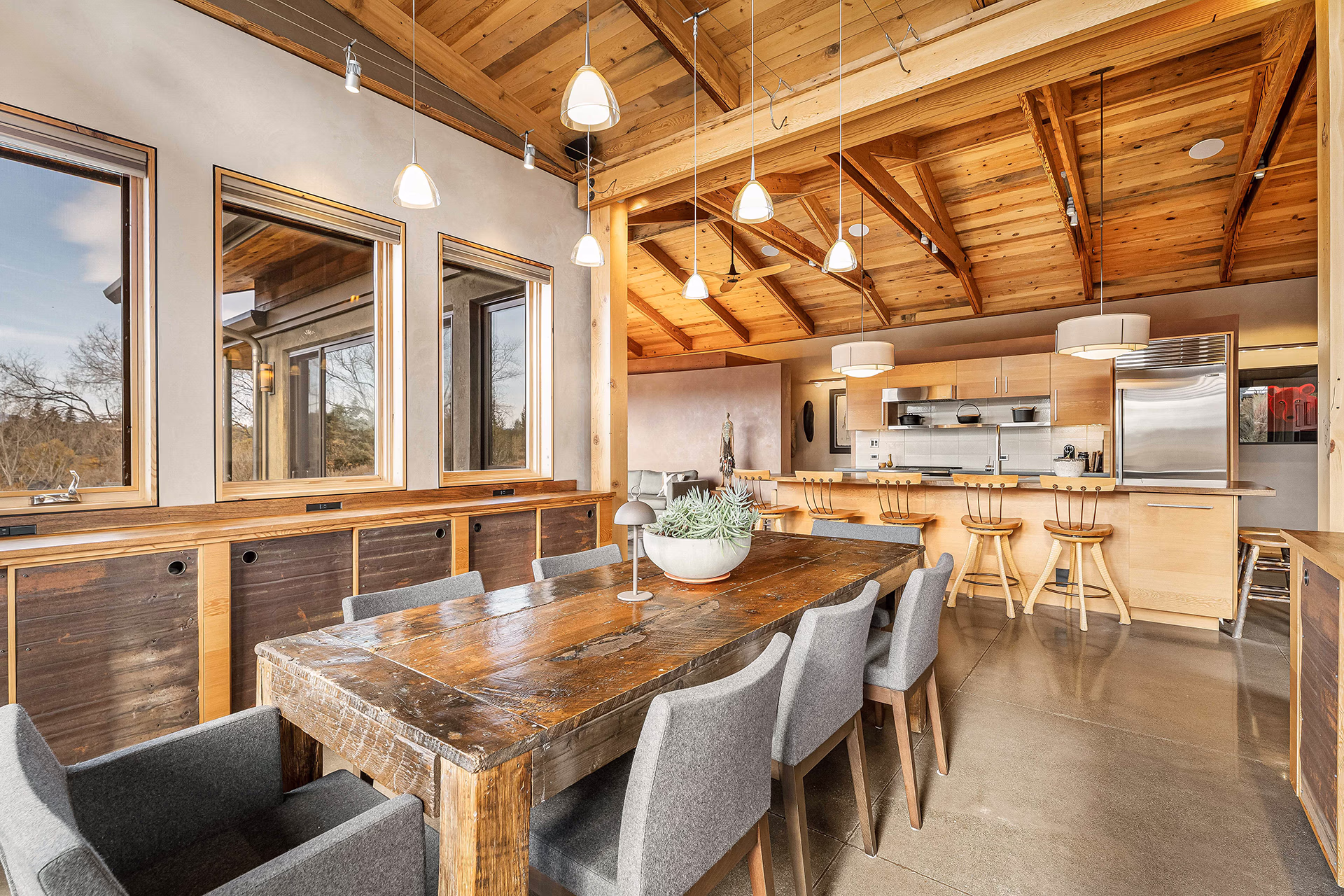 Dining room and kitchen with reclaimed wood table, wood ceiling beams and large windows in a sustainable Bend home