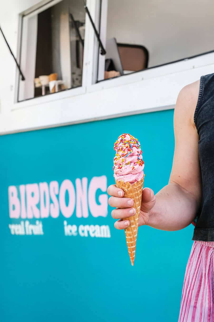 A woman holding an ice cream cone in front of a turquoise ice cream truck