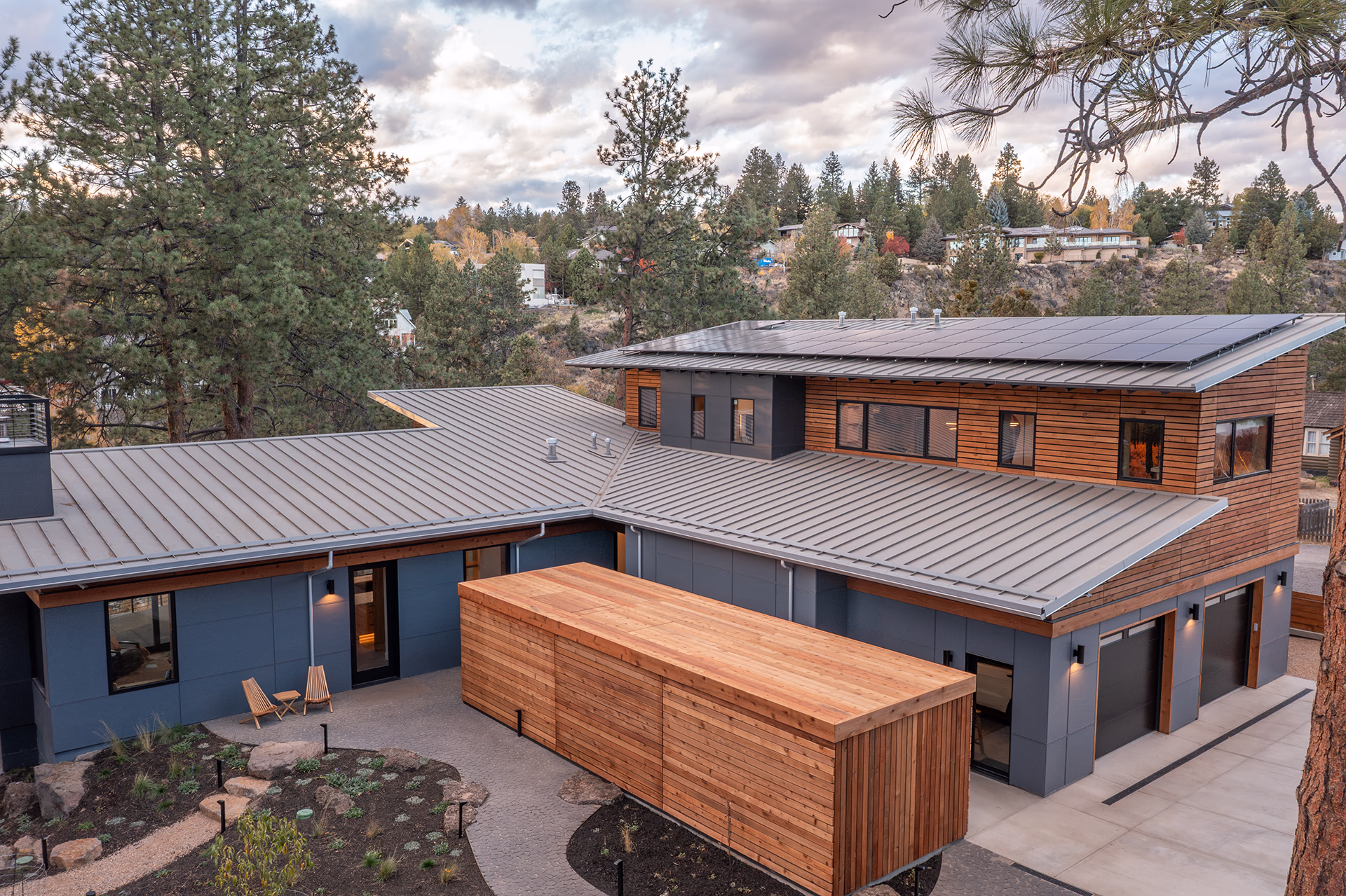 Modern Bend home with large rooftop solar array, metal roof and wood siding overlooking trees and neighborhood.