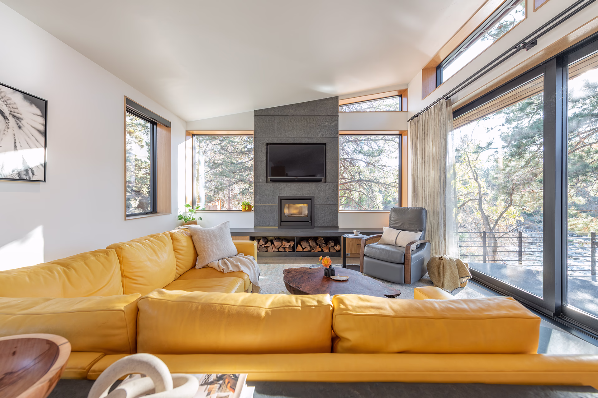 Bright living room with yellow sectional sofa, wood-trimmed windows and forest views in a modern Bend home.