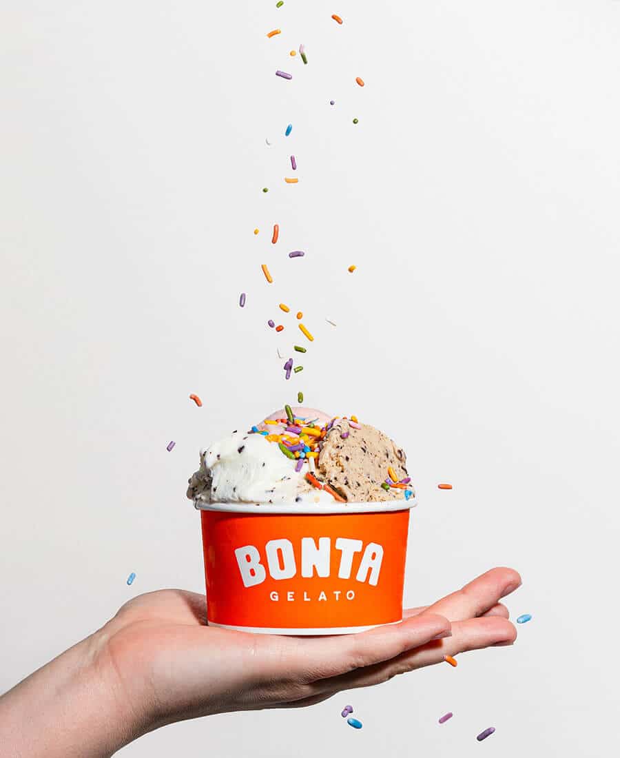 hand holdinga cup of bonta gelato with sprinkles falling from above onto it